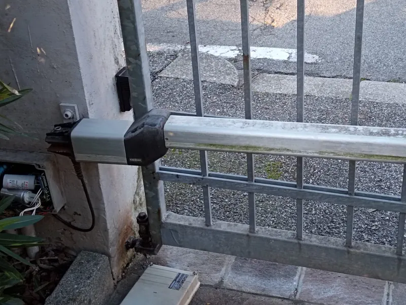Attuatore a pistone su cancello battente, con la centrale di comando aperta accanto al pilastro